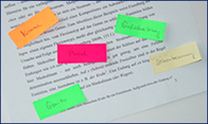 Korrektur einer Bachelorarbeit: Foto mit bunten Zetteln auf einem bedrucktem Blatt zum Thema